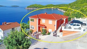 Une propriété située sur la côte, avec une maison au toit rouge, une voiture blanche et une vue sur la mer et les îles.