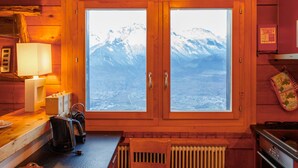 A cozy cabin interior with wooden walls, a large window with a mountain view, a kitchen area with a kettle, and a radiator. - Crettamour by Interhome (Veysonnaz)