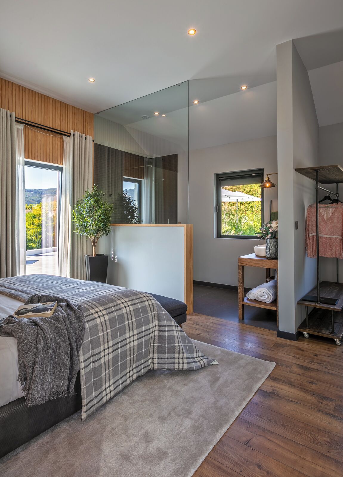 Une chambre à coucher moderne avec un grand lit, une table de chevet, un miroir et une vue sur l’extérieur.