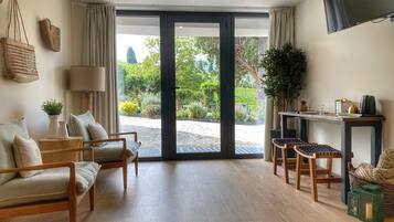 A spacious living room with a large sliding glass door leading to a garden, a wooden coffee table, a sofa, and a small side table with a lamp.