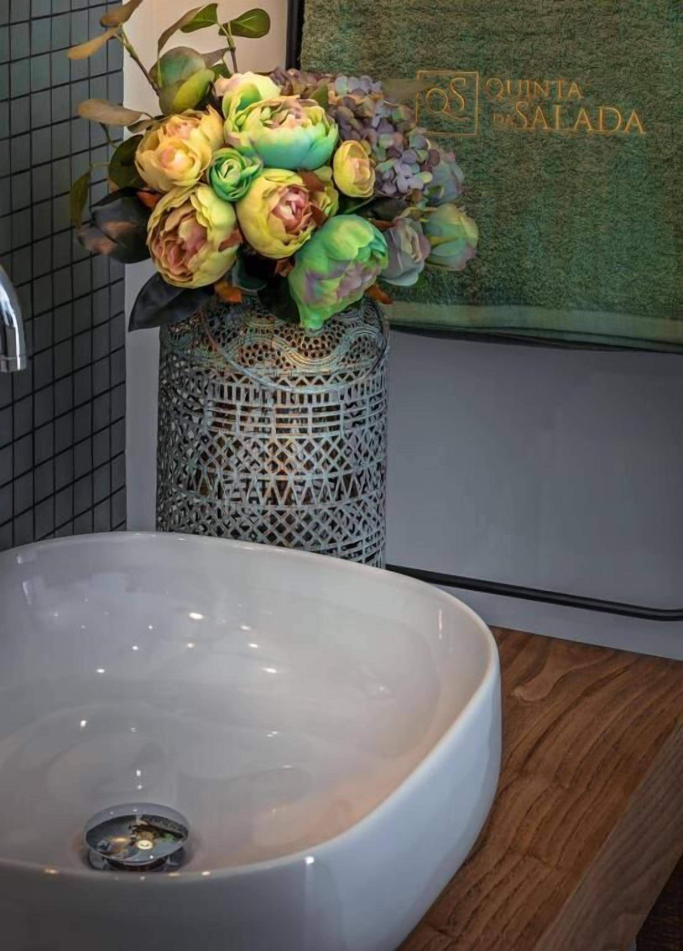 Un baño con un lavamanos blanco, un jarrón decorativo con flores y una pared verde con un letrero.