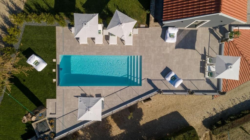 Luftaufnahme eines Poolbereichs mit Liegestühlen und Sonnenschirmen.