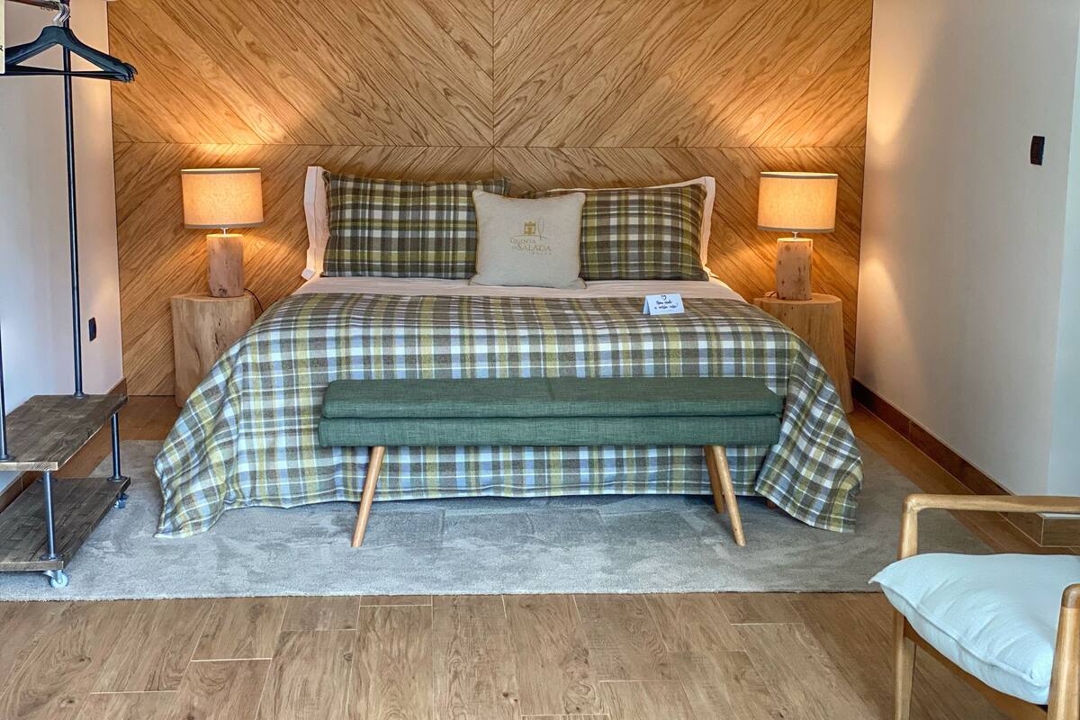 A neatly arranged bedroom with a plaid bedspread, matching pillows, and a bench.