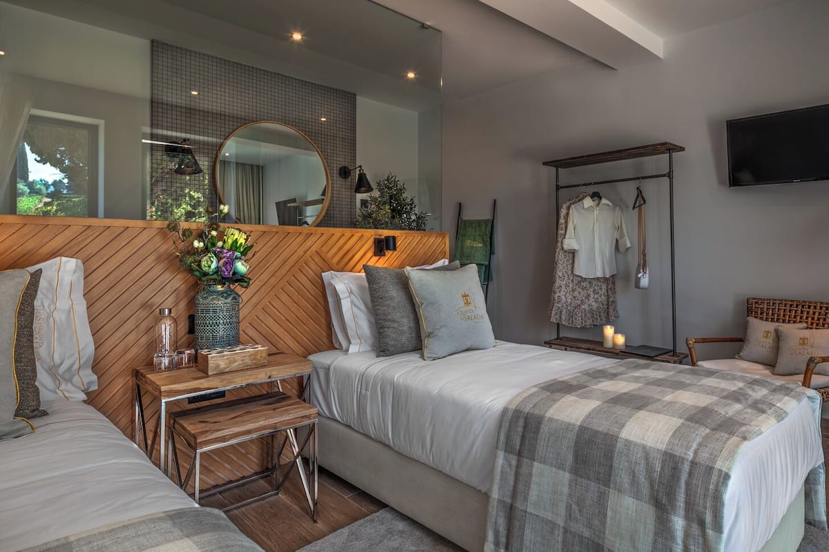 A modern bedroom with a large bed, bedside tables, a mirror, a TV, and a wardrobe.