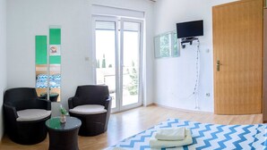 A hotel room with a bed, two wicker chairs, a small table, a TV mounted on the wall, and a sliding glass door leading to an outdoor area. - Apartments Smokvica - One Bed/Apt with Balcony (Starigrad-Paklenica)