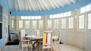 Ein Essbereich mit einem runden Tisch und Stühlen, großen Fenstern mit Fensterläden und einer blauen Decke.