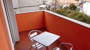 En balkon med et bord og stole, der kigger ud over et boligområde med huse og grønt.