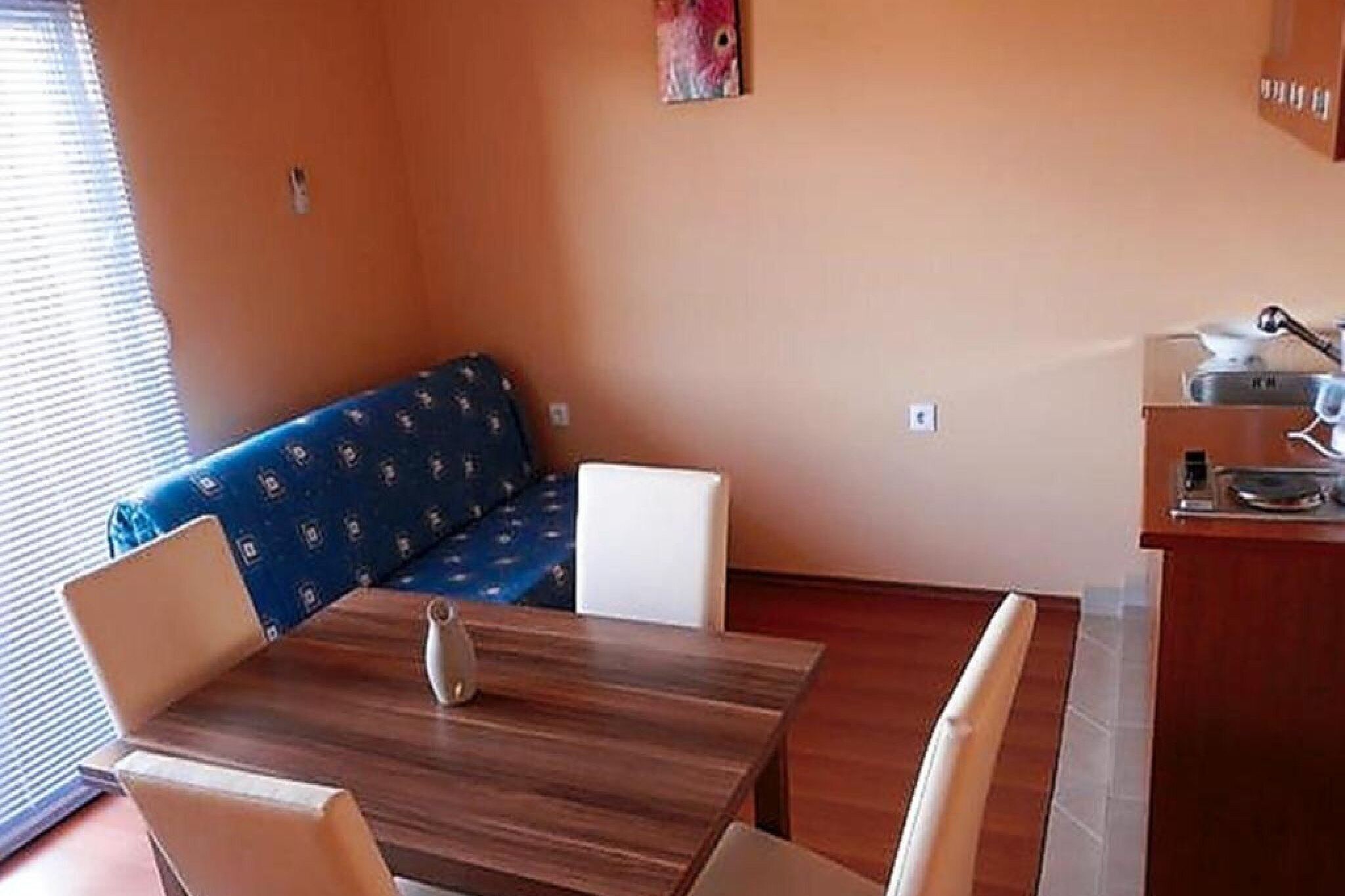 Een knus kamertje met een houten eettafel, een blauwe gestreepte bank en een kleine kitchenette.