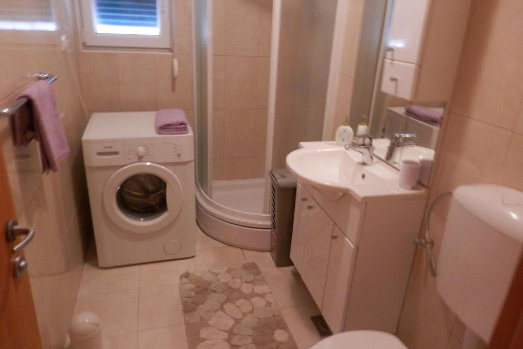 Ein kleines Badezimmer mit Waschmaschine, Dusche, Waschbecken und Toilette.