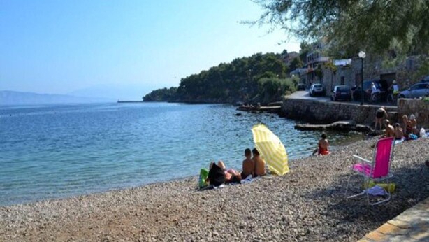 A pebbled beach with people relaxing under umbrellas, a stone wall, and a view of the sea. - Apartments St Rialto - Comfort One-Bedroom Apartment with Balcony and Sea View (Jelsa)