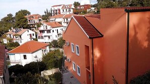 A residential area with terraced houses, a prominent orange building, and a hillside backdrop. - Apartments St Rialto - Comfort One-Bedroom Apartment with Balcony and Sea View (Jelsa)