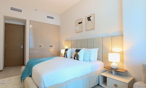 A hotel room with a bed, bedside tables, a nightstand, a door, and two wall-mounted air vents.