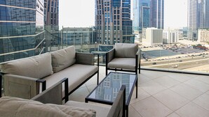 A balcony with a sofa and chairs, offering a view of a cityscape with tall buildings and a busy road. - Spacious 1BR Apt Designed by Missoni (Dubai)
