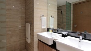 A modern bathroom with two sinks, a glass shower enclosure, and a wooden vanity. - Spacious 1BR Apt Designed by Missoni (Dubai)