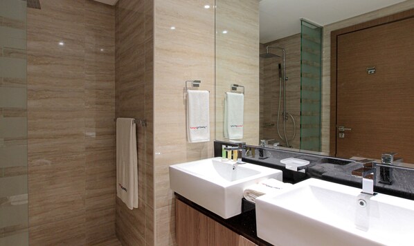 A modern bathroom with two sinks, a glass shower enclosure, and a wooden vanity. - Spacious 1BR Apt Designed by Missoni (Dubai)