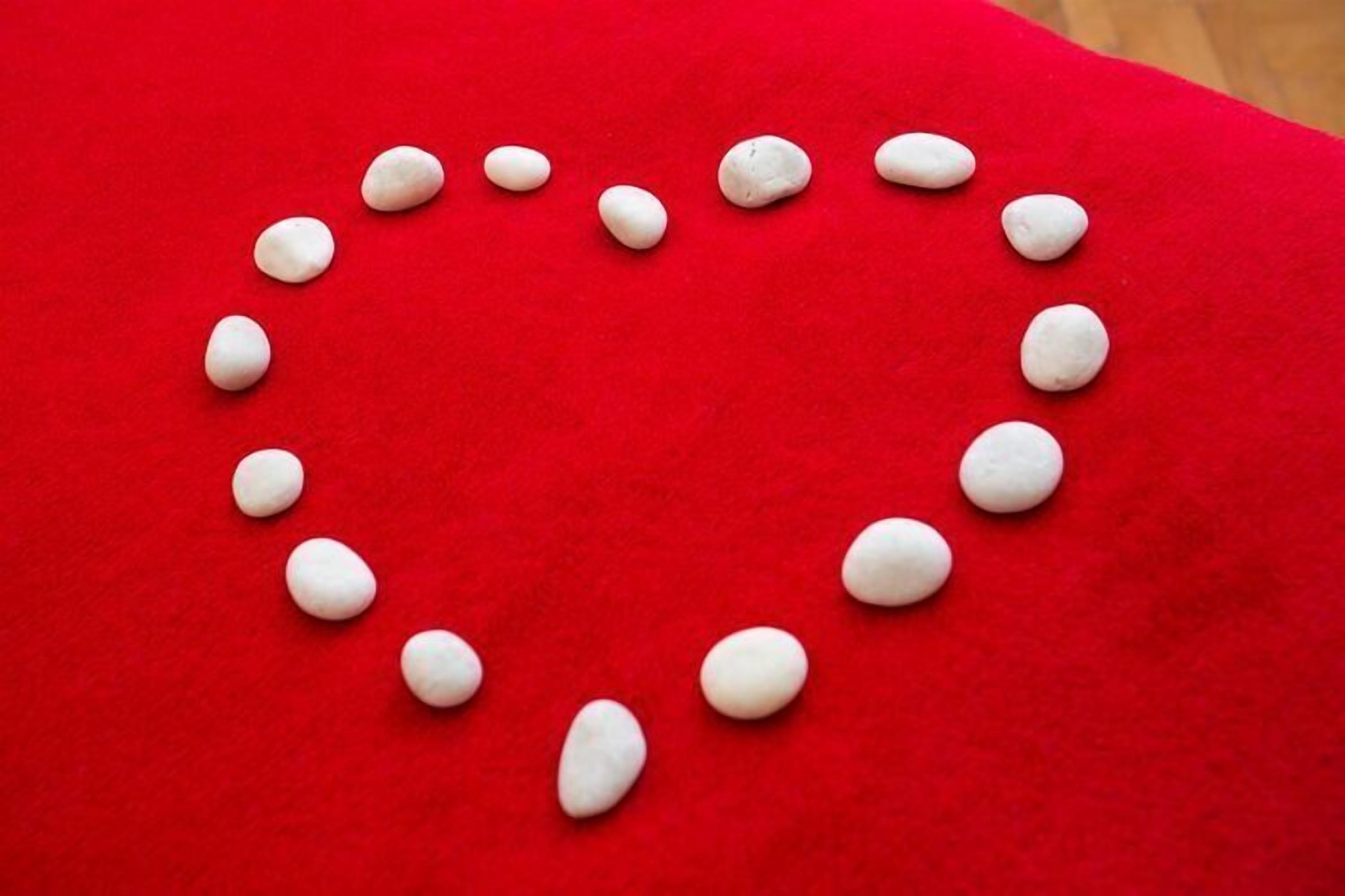 A heart-shaped arrangement of white stones on a red surface.