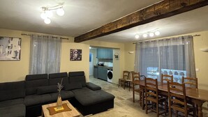 Una sala de estar con un sofá, una mesa de centro y un comedor con mesa y sillas. Se ve una cocina al fondo.