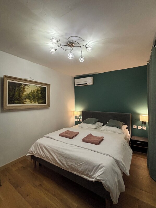 Ein Schlafzimmer mit einem Bett, Nachttischlampen, einer Klimaanlage, einem gerahmten Gemälde und Holzboden.