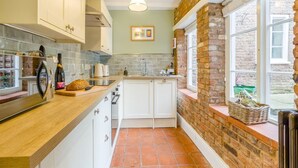A compact kitchen with white cabinets, a wooden countertop, a tiled backsplash, and a brick wall. - Papist Hall Cottages (Barrow upon Humber)