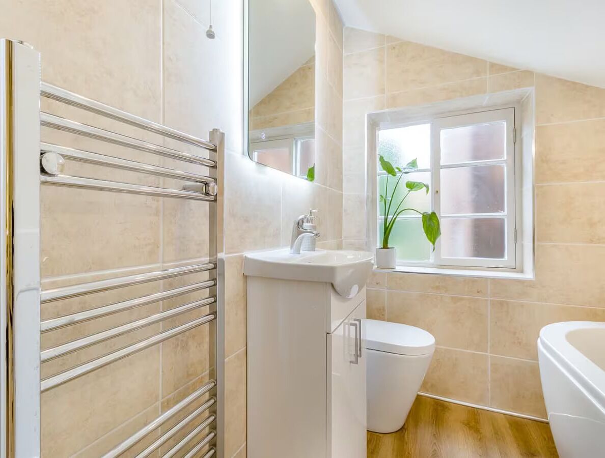 A bathroom with a white sink, toilet, and bathtub, a towel rack, and a window with a plant.