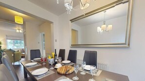 A dining area with a long table set for four, a chandelier, and a large mirror on the wall. - Parlaunt House - 3 bedroom with FREE Parking (Langley)