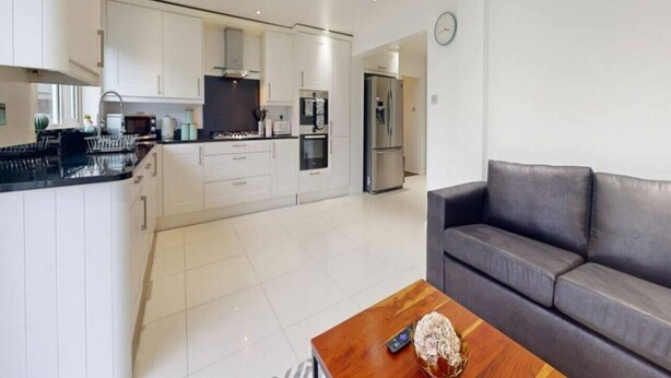 A modern kitchen with white cabinets, stainless steel appliances, and a wooden dining table with a remote control. - Parlaunt House - 3 bedroom with FREE Parking (Langley)