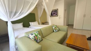 A room with a bed, a green sofa, a wooden table, and a wardrobe. - Luxury 2 Story Loft in Boutique Lodge 2 With Free Savannah Adventure 4x4 Tour (Victoria Falls)