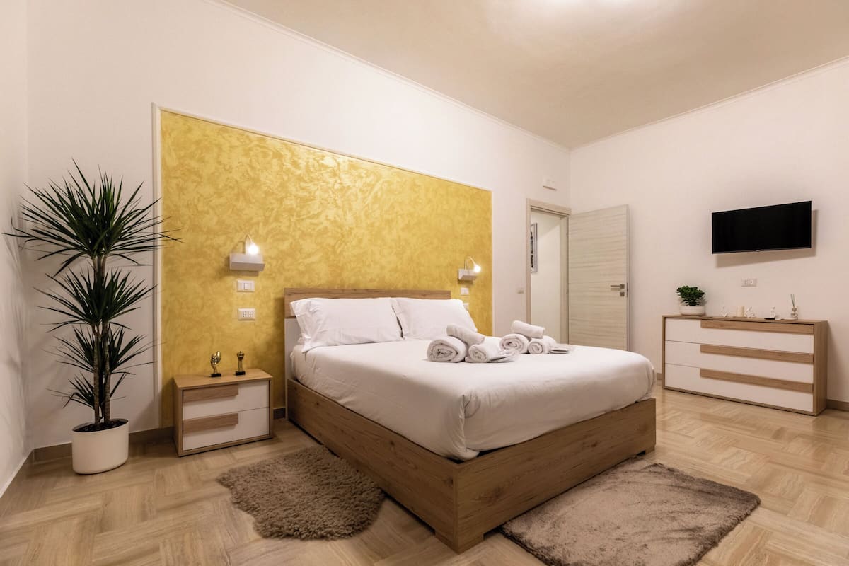 Een slaapkamer met een houten bed, nachtkastjes, een televisie en een potplant.