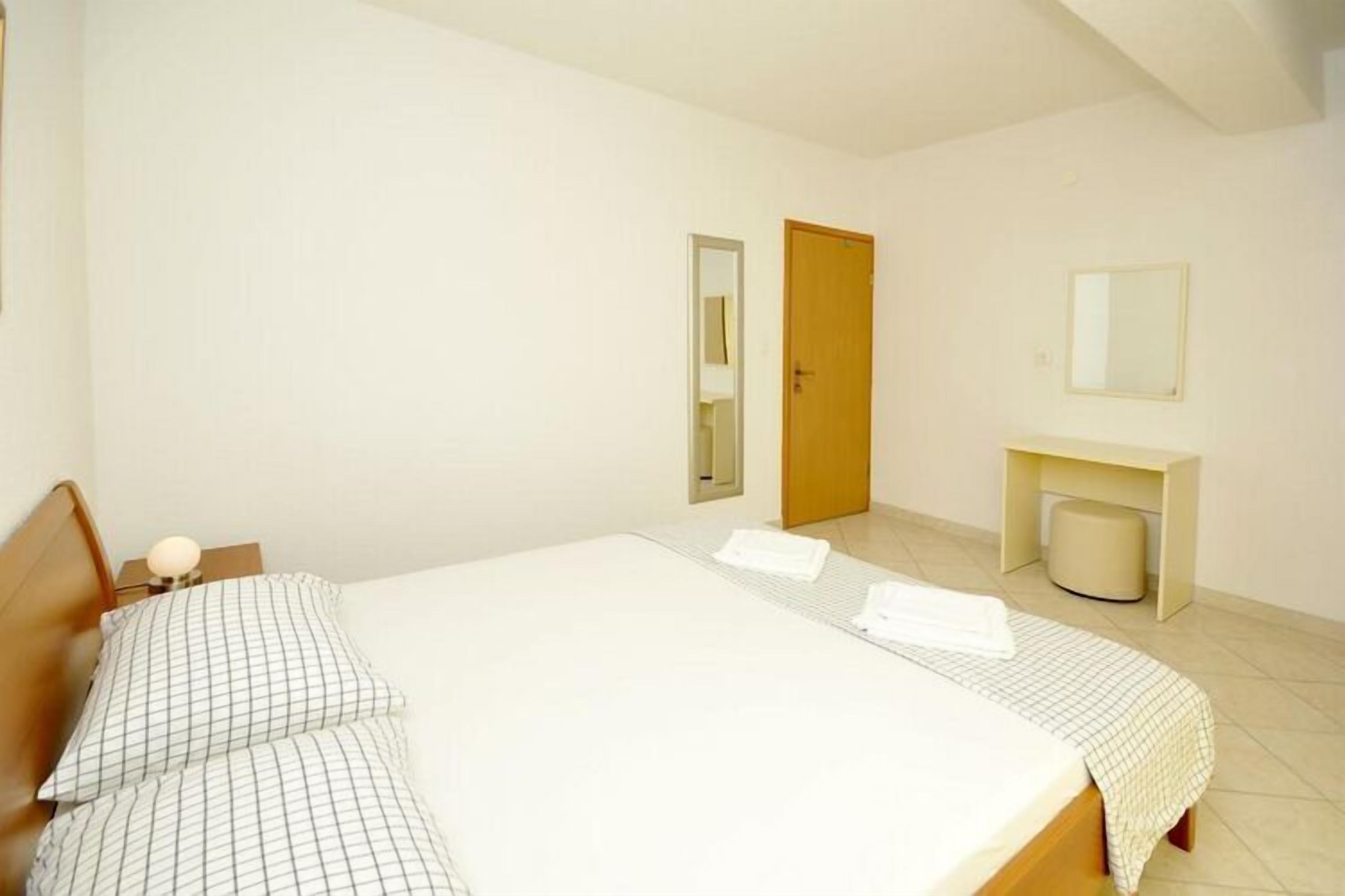 Une chambre d’hôtel propre et bien éclairée, avec un grand lit, une table de chevet avec une lampe, un petit bureau avec une chaise et un miroir au mur.