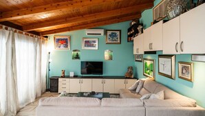 Un salon avec un plafond en bois, des murs de couleur turquoise, un canapé beige, un téléviseur et divers tableaux encadrés.
