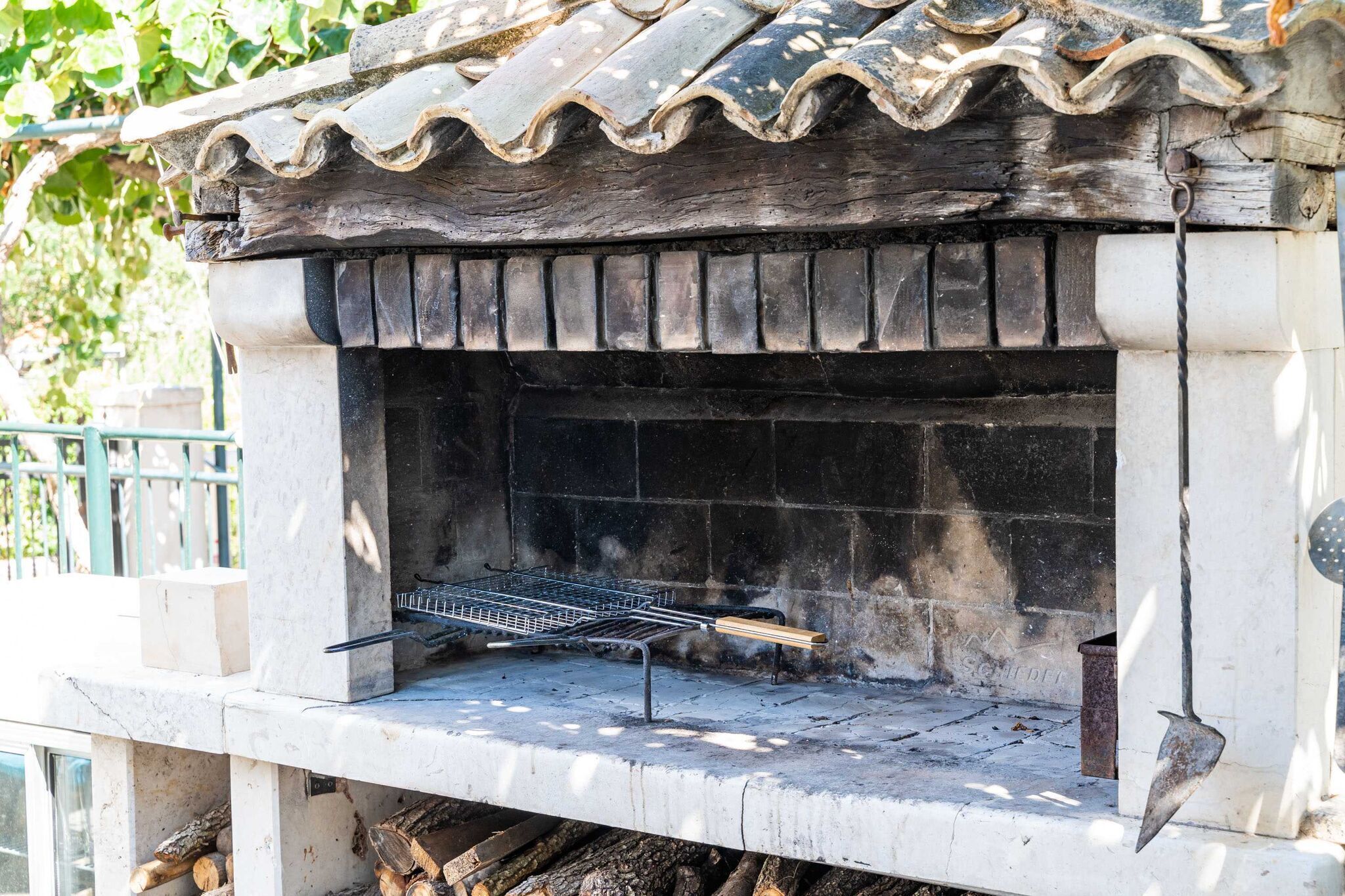 A traditional stone-built outdoor oven with a tiled roof, a metal rack for grilling, and a firewood storage area beneath.