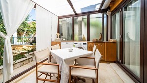 Une terrasse ensoleillée avec une table et des chaises, un lave-linge et un coin cuisine équipé de placards et d’une fenêtre.