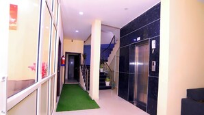 Un'hall d'albergo con tappeto verde, una scala e un ascensore.