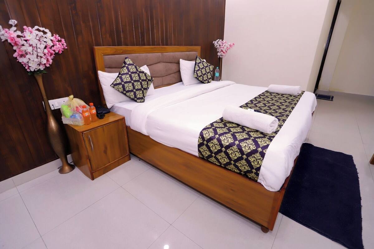 A neatly made bed with patterned bedspreads, a wooden nightstand with toiletries, and a dark rug.