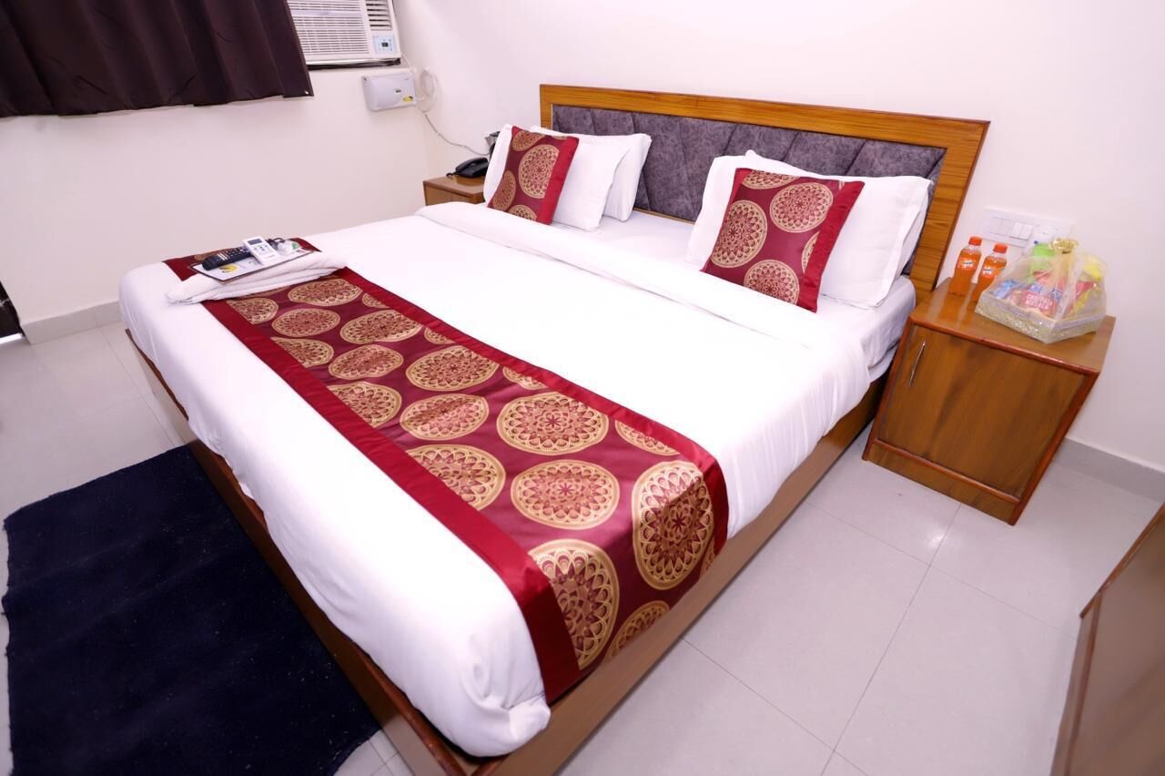 A neatly made bed with a patterned bedspread, a bedside table with a bottle of water, and a small nightstand with a phone and a remote control.