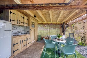 Una cocina campestre al aire libre con armarios de madera y estufa empotrada, rodeada por una valla de madera y una pequeña mesa con sillas.
