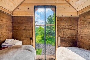 Habitación de cabaña de madera con dos camas, un ventanal grande y vistas de la vegetación.