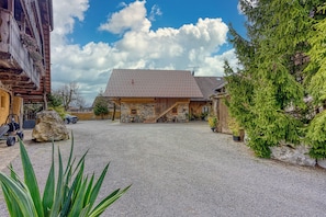 Un bâtiment rustique en pierre, doté d’un porche en bois et d’une allée gravillonnée.