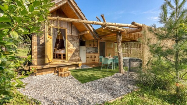 A wooden cabin with a stone exterior, a covered outdoor seating area, and a gravel driveway.