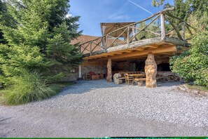 A rustic wooden structure with a stone foundation, a covered outdoor area with seating, and a gravel driveway. - Luxury Glamping House Pia (Ivančna Gorica)