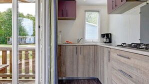 A compact kitchen with wooden cabinets, a gas stove, and a window with blinds. - 6 Person Holiday Park Home in Jelling (Jelling)