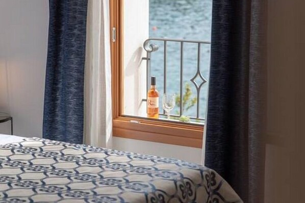 A hotel room with a bed, a window with a view of the sea, and a bottle of wine on the windowsill.