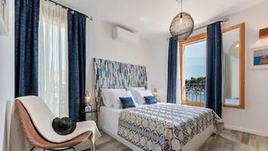 A bedroom with a bed, a chair, a nightstand, and a large window with curtains.