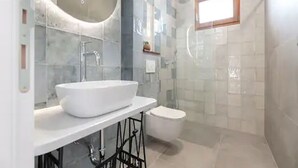 A modern bathroom with a large white sink, a glass shower enclosure, and a small window.
