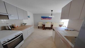A modern kitchen with white cabinets, a built-in oven, and a dining area with a table and chairs.