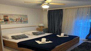 A modern hotel room with a large bed, a ceiling fan, a painting on the wall, and a window with curtains.