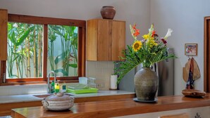 A kitchen with wooden beams, a large window with a view of greenery, a vase with flowers, and two bar stools. - Yans Family Villa Canggu by Betterplace (Canggu)