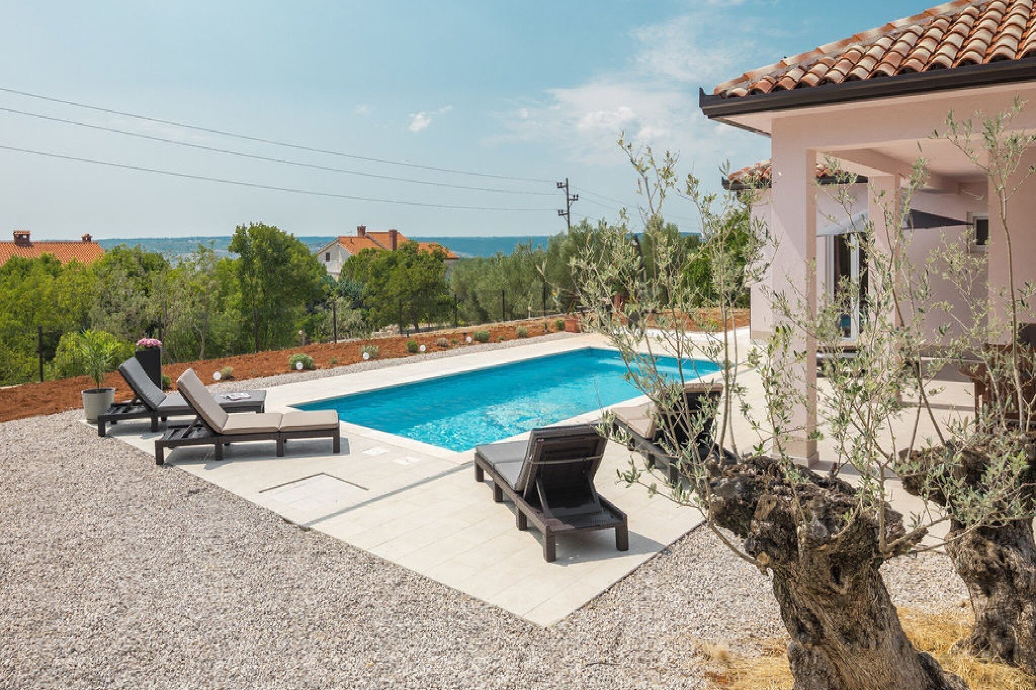 A swimming pool with lounge chairs, a view of the sea, and a building with a tiled roof.