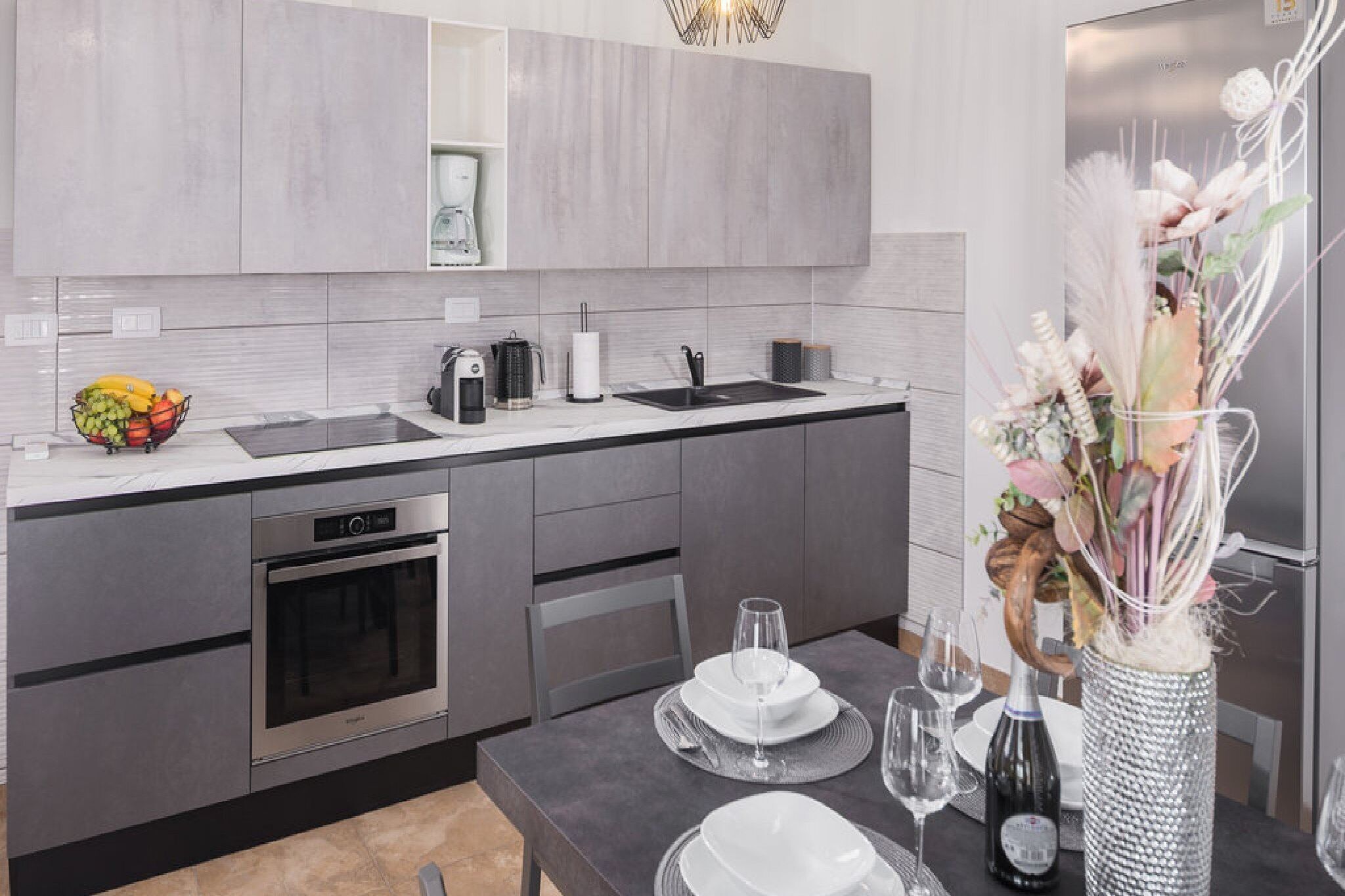 A modern kitchen with grey cabinetry, a black countertop, and a dining area set with white plates and glasses.
