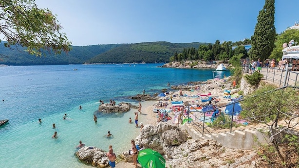 Une scène de plage côtière avec une eau claire, un rivage rocheux et des personnes qui se baignent.